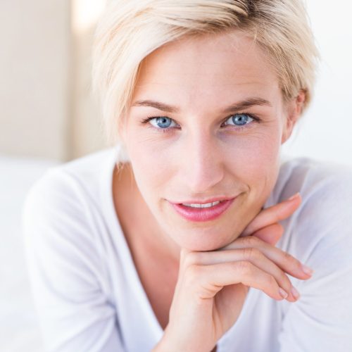 Smiling blonde woman lying on the bed and looking at camera in her bedroom